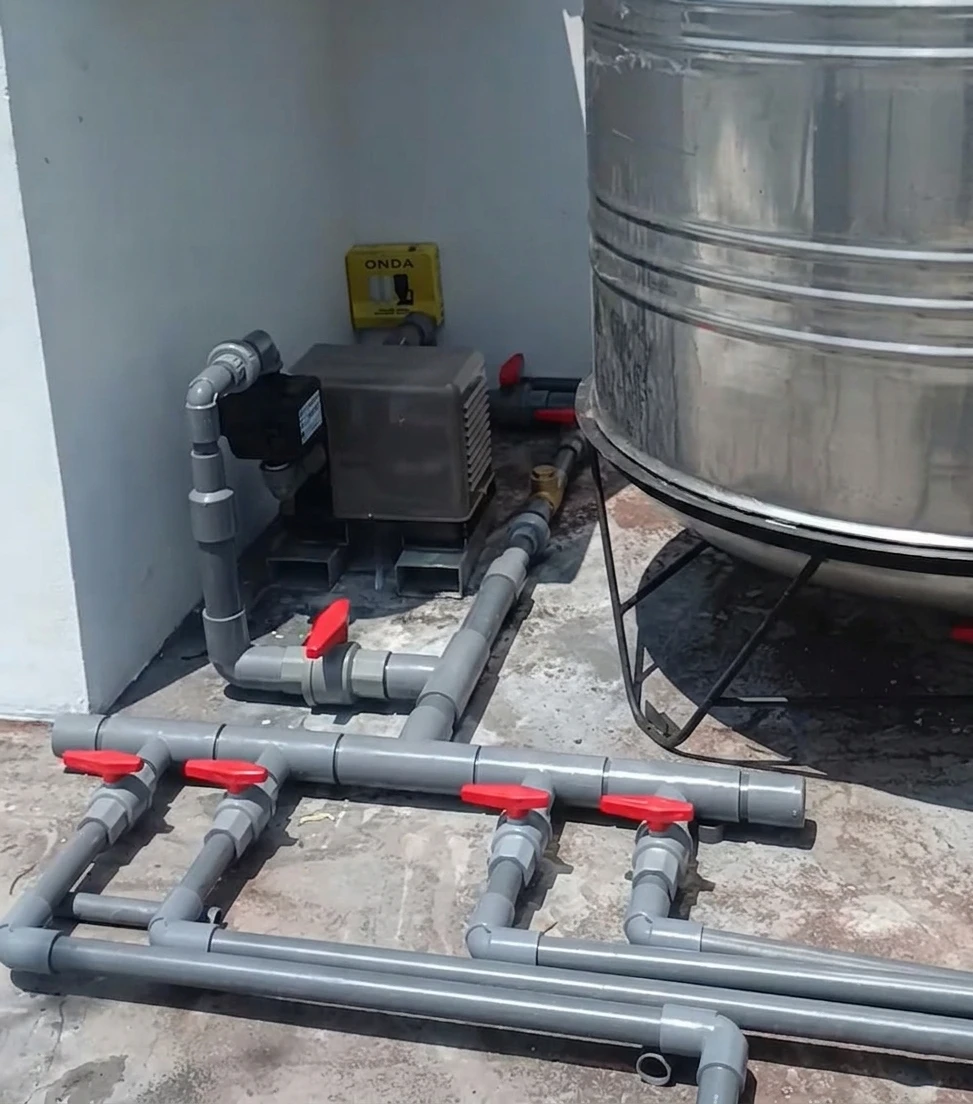 Instalasi pipa PVC abu-abu dengan pompa dan toren air