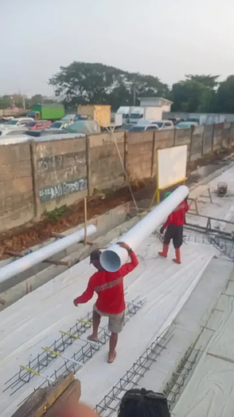 Pekerja memikul batang pipa PVC Gavin di atas lantai kerja saluran drainase trotoar Meruya